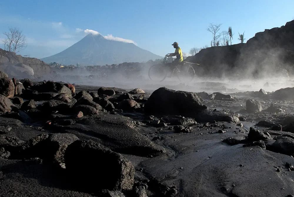 Alur sungai penuh batu hitam bekas lahar, dengan gunung api di kejauhan